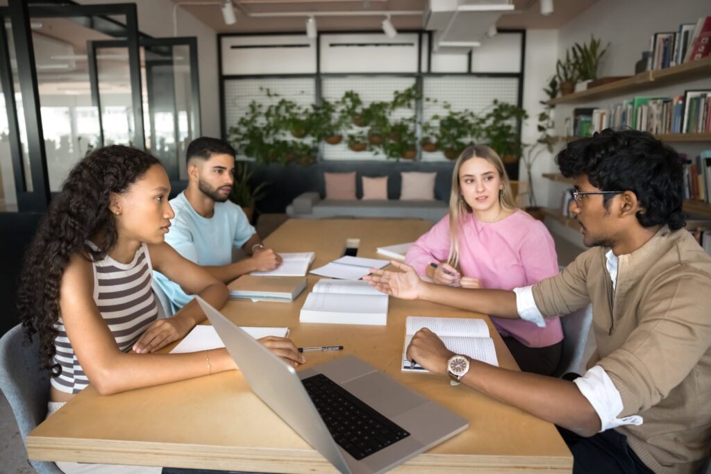 Group of students researching, studying together gathered in library, listening Indian teammate express point, solution or opinion, working on essays, tasks, or creative projects. Teamwork, education
